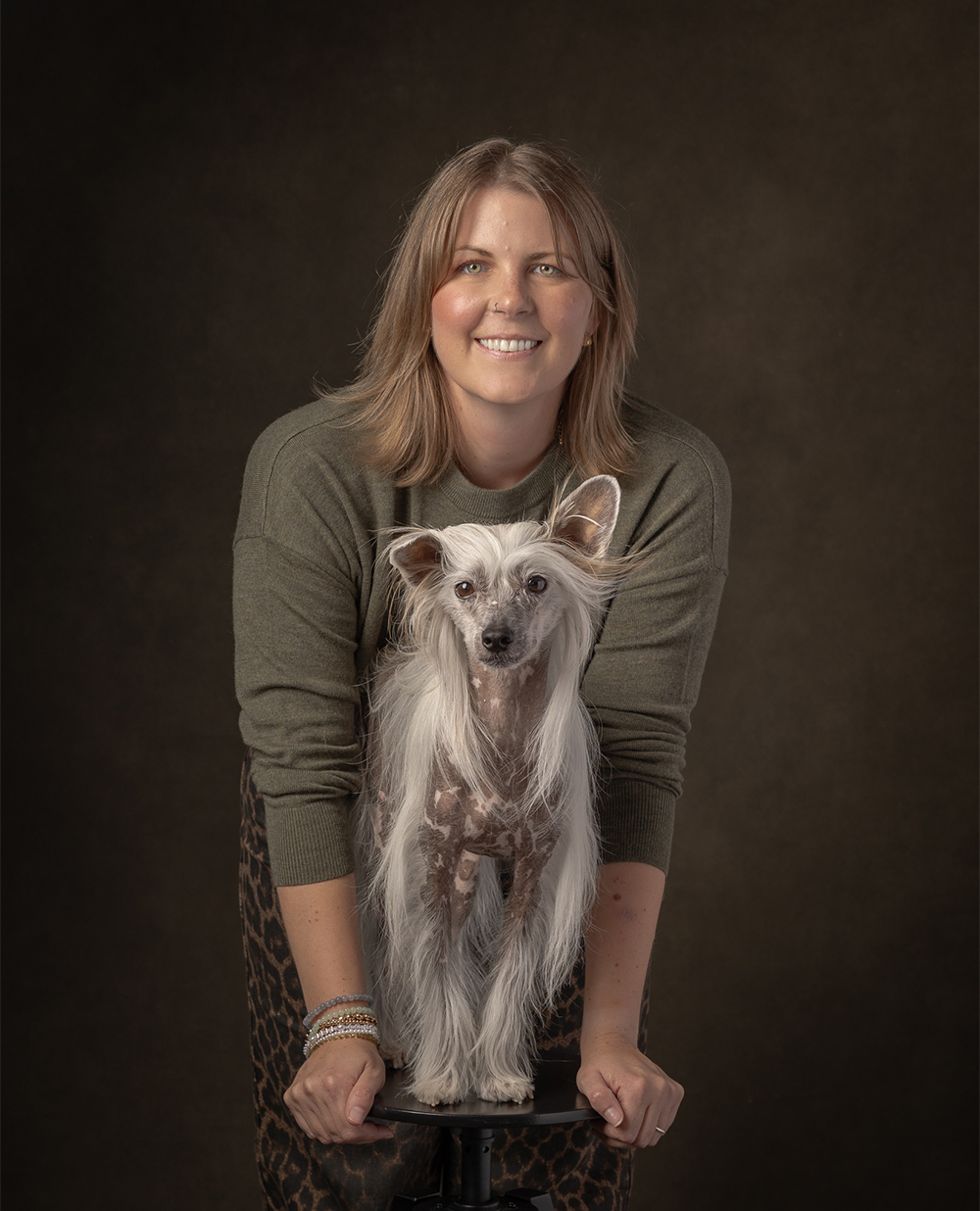 Young couple wearing fall clothes against wood wall hugging their pointer and smiling